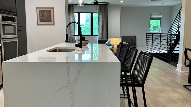 Een moderne keuken met een groot marmeren eiland, zwarte barkrukken en uitzicht op een trap.