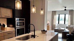 Een moderne keuken met een groot eiland, inbouwovens en hanglampen.