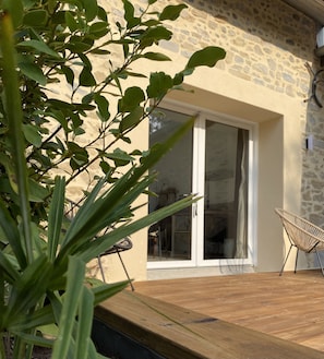 A wooden deck with a stone wall and a glass door leading to an interior space.