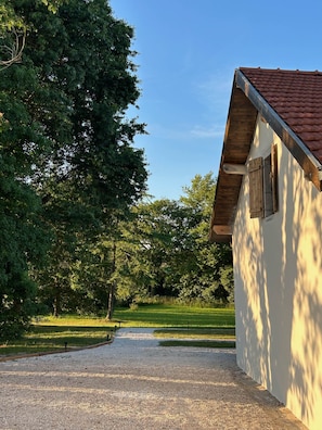 A gravel path leading to a building with a red-tiled roof and wooden shutters.