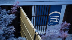 Ein traditionelles japanisches Tor mit einem blauen Schild mit weißen Schriftzeichen.