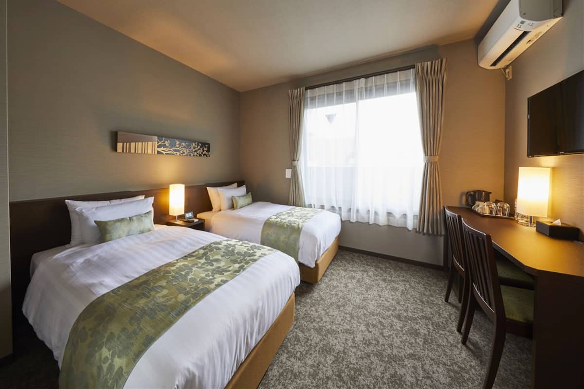 Habitación de hotel con dos camas, un escritorio, una silla, un televisor y una ventana con cortinas.