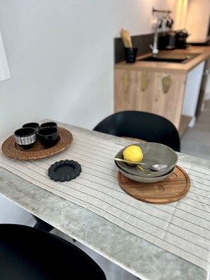 Een keuken met een houten aanrecht, een spoelbak en een fornuis. Op een geweven mat staan vier zwarte bekers, een kom met een citroen, en een zwart decoratief object op het aanrecht.