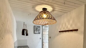 A narrow hallway with a rustic ceiling, a hanging light fixture, a radiator, and a framed picture on the wall. - Sunset by FY (Josse)