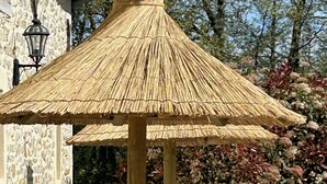 A thatched gazebo with a wooden frame, surrounded by lounge chairs and a stone wall. - Sunset by FY (Josse)