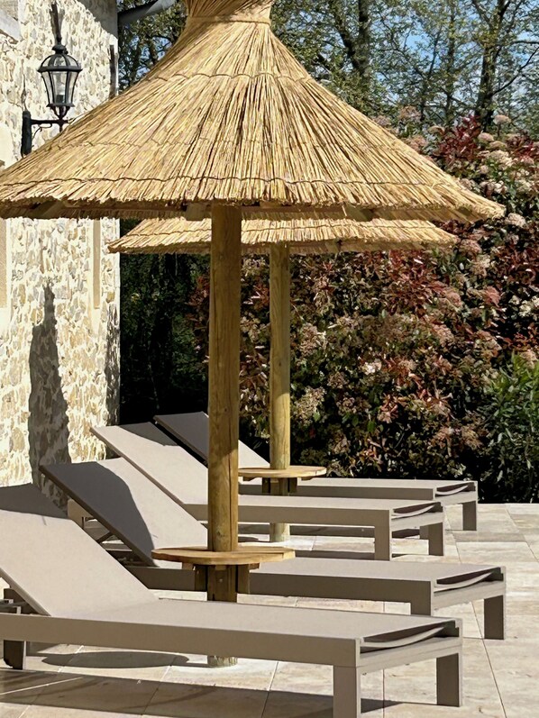 A thatched gazebo with a wooden frame, surrounded by lounge chairs and a stone wall. - Sunset by FY (Josse)