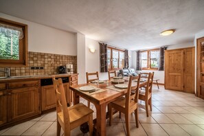 Une cuisine avec des meubles en bois, une table à manger dressée pour quatre personnes et une vue sur l’extérieur grâce à de grandes fenêtres.