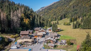 Un pueblo de montaña con casas de madera tradicionales, un edificio central con tejado inclinado y una vista despejada del bosque y las colinas circundantes.