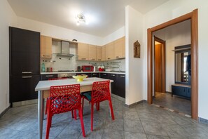 Une cuisine moderne avec un coin repas, comprenant une table blanche, des chaises rouges et un four à micro-ondes.