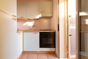 Une cuisine compacte avec des meubles blancs, un four encastré et un plan de travail doté d’une plaque de cuisson.