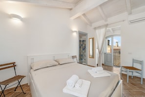 A bedroom with a bed, a bench, a chair, and a view of the outside.