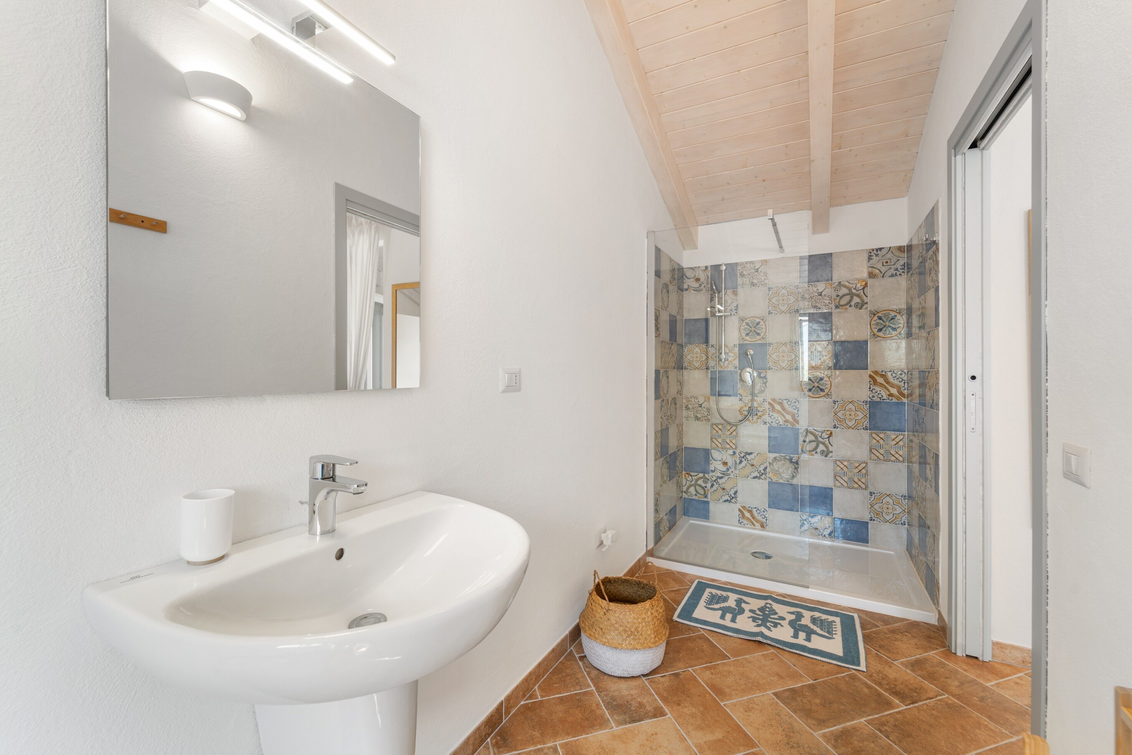 A bathroom with a sink, mirror, shower, and tiled floor.