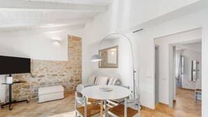 A modern living room with a stone wall, a round table with chairs, a flat-screen TV, and a large floor lamp. - Holiday Home 'La Casetta' with Private Terrace, Wi-Fi and Air Conditioning (Giba)