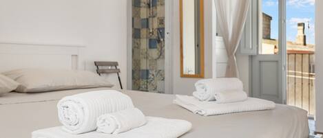 A hotel room with a bed, two rolled towels, a shower, a bathroom mirror, and a view of the outside.