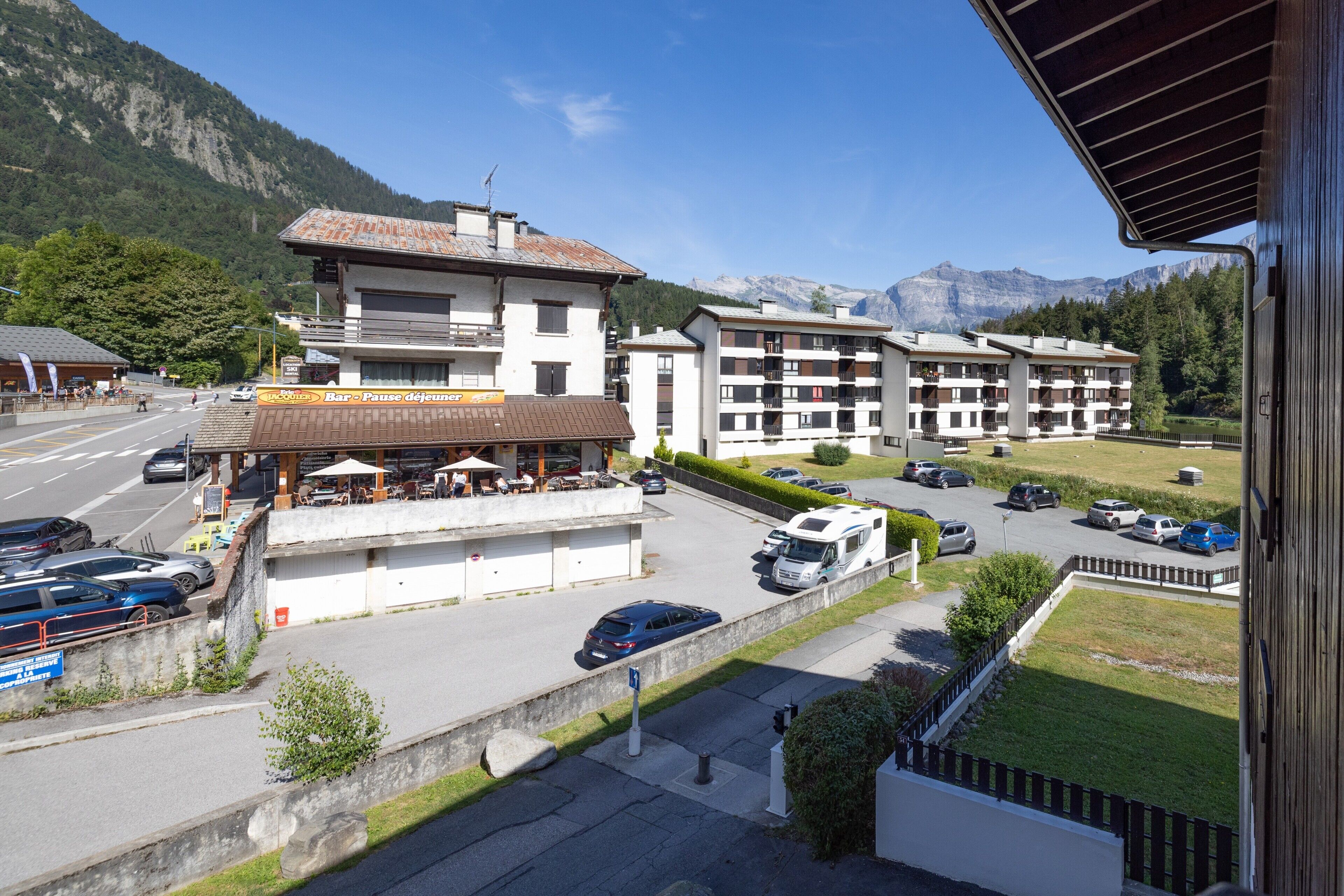 A hotel with multiple floors, outdoor seating, and a parking area with cars.