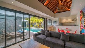 A modern living room with a gray sofa, wooden coffee table, and a glass door leading to a pool area. - Villa Yasmee (Seminyak)