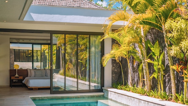 A modern pool area with a glass-enclosed bedroom and tropical plants. - Villa Yasmee (Seminyak)