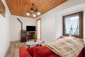 A room with a wooden ceiling, a television, a red sofa, a window with a view, and a small table with a plant. - Apartment "Casa del Sole" with Mountain View & Wi-Fi (Toceno)