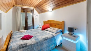A bedroom with a sloped ceiling, a bed with a patterned bedspread, a nightstand with a lamp, and a window with curtains. - Apartment "Casa del Sole" with Mountain View & Wi-Fi (Toceno)
