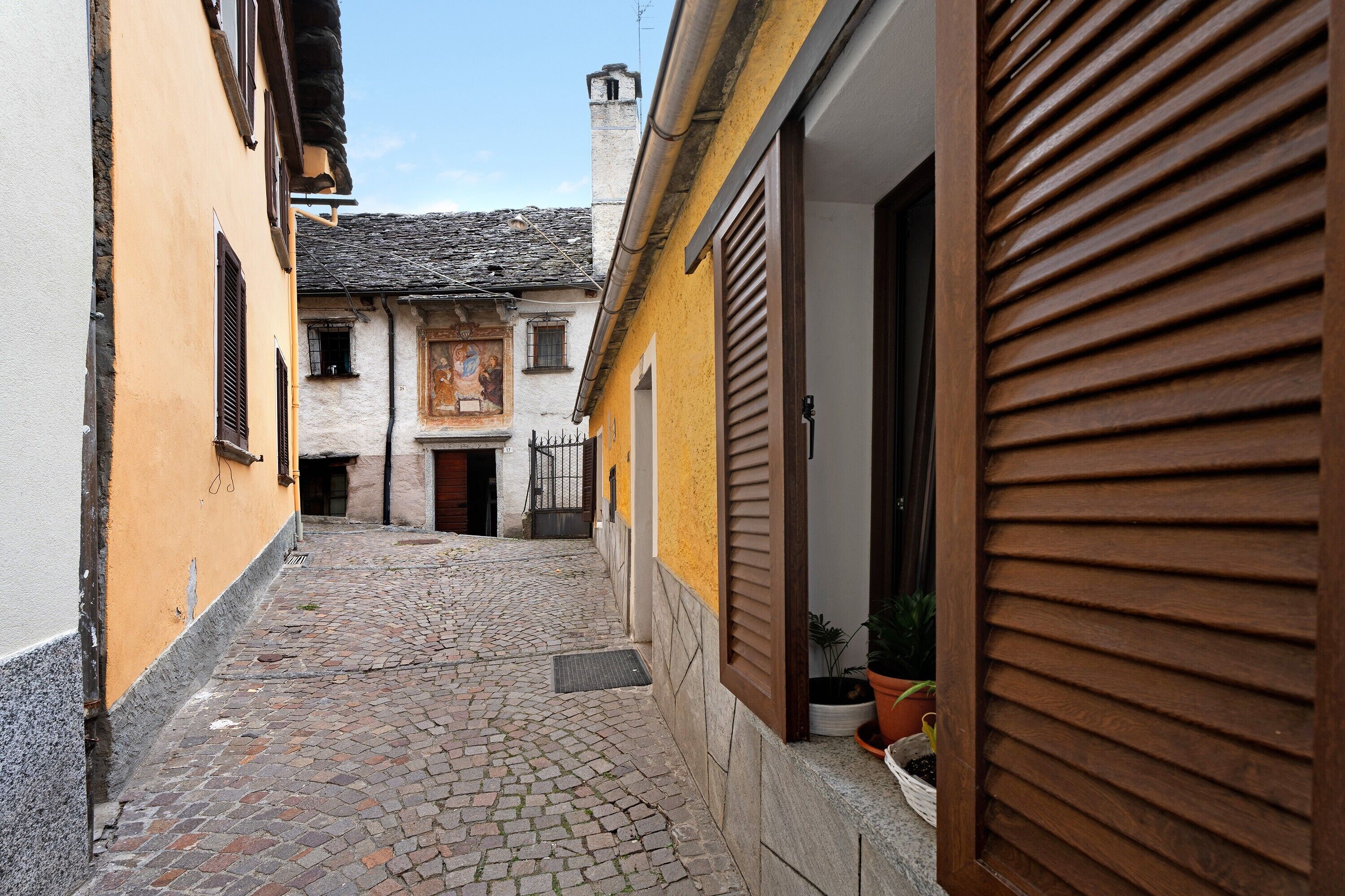 Una estrecha calle adoquinada entre edificios con fachada amarilla y persiana de madera.