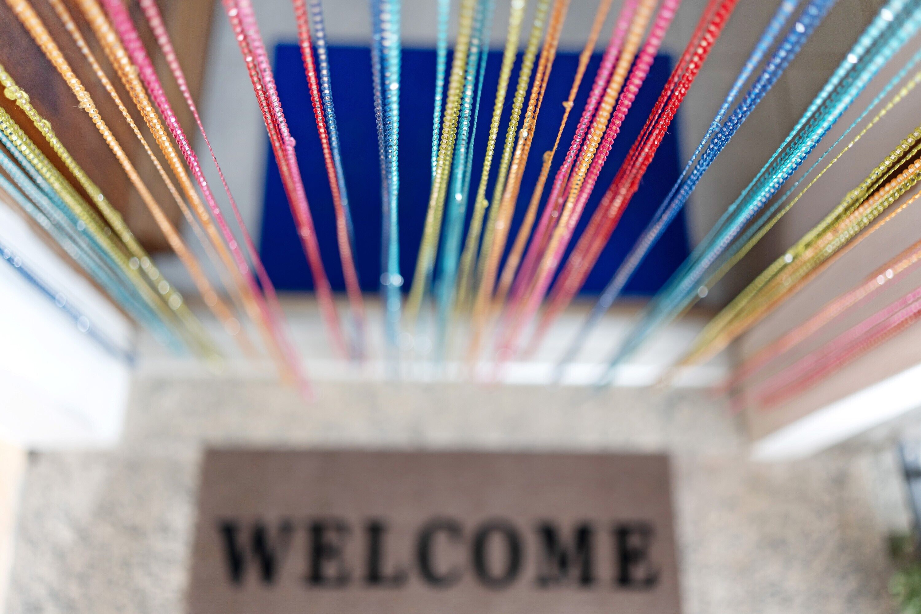 Ein Detailaufnahme eines Schildes mit der Aufschrift 'WELCOME' und farbenfrohen Bändern.
