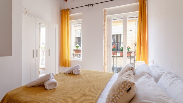 Una habitación de hotel con cama, armario y balcón con cortinas amarillas.