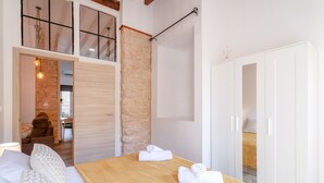 Un dormitorio con cama, cabecera de madera, pared de piedra, armario y baño visible a través de una puerta abierta.