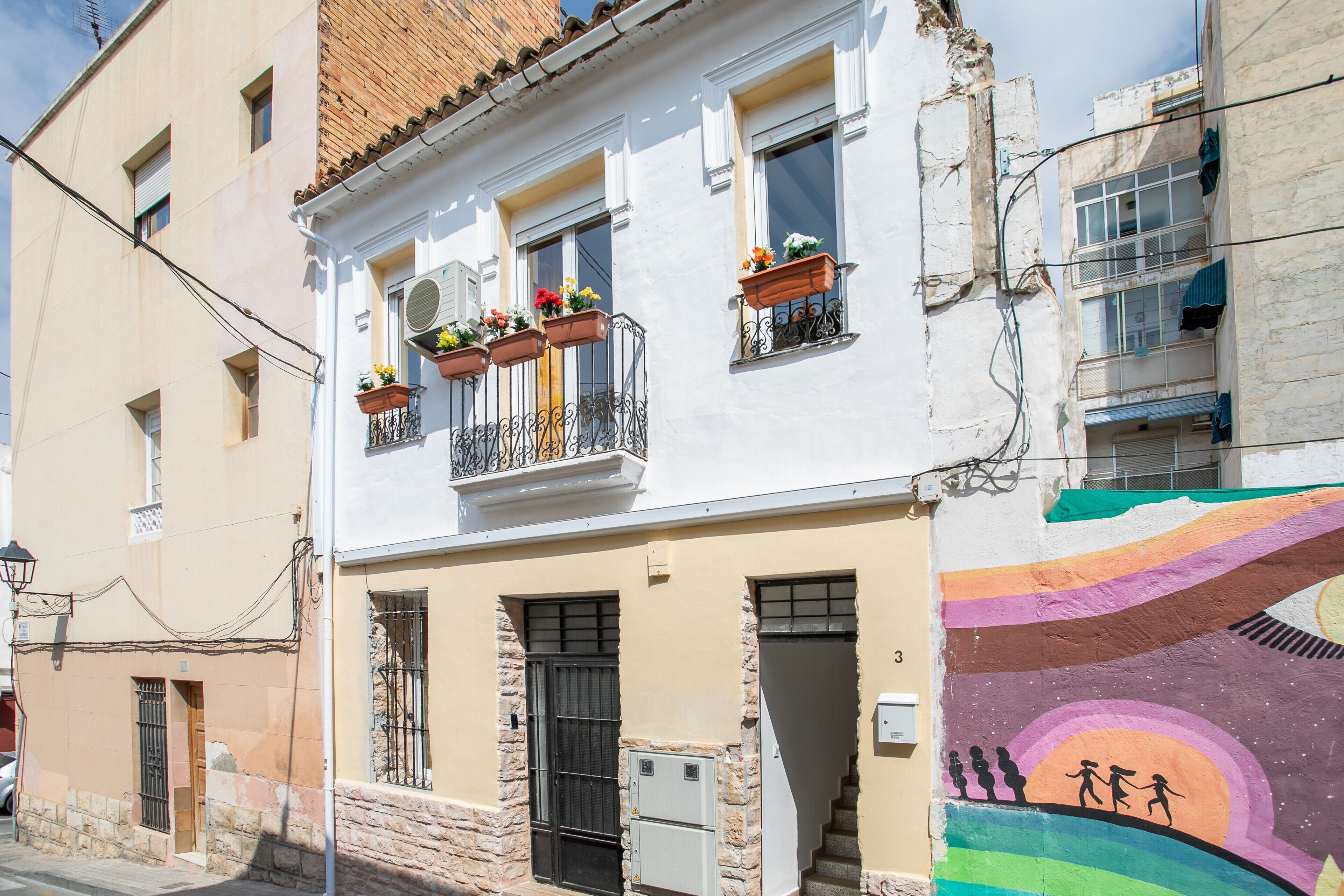 A building with a white facade, a balcony with flower boxes, and a colorful mural on the right side.