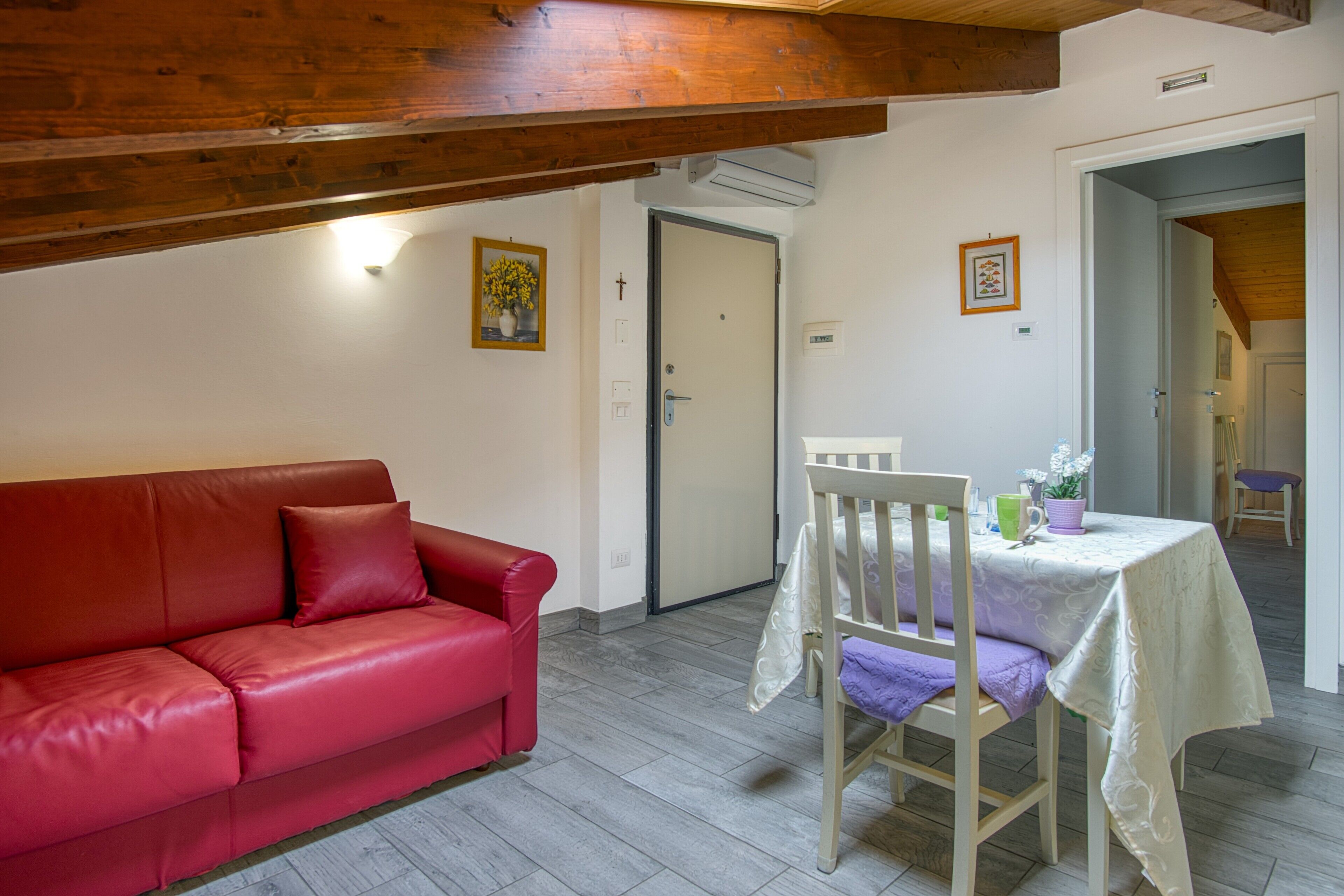 A red leather sofa, a small table with a white tablecloth, and a wooden chair in a room with a wooden ceiling and white walls.