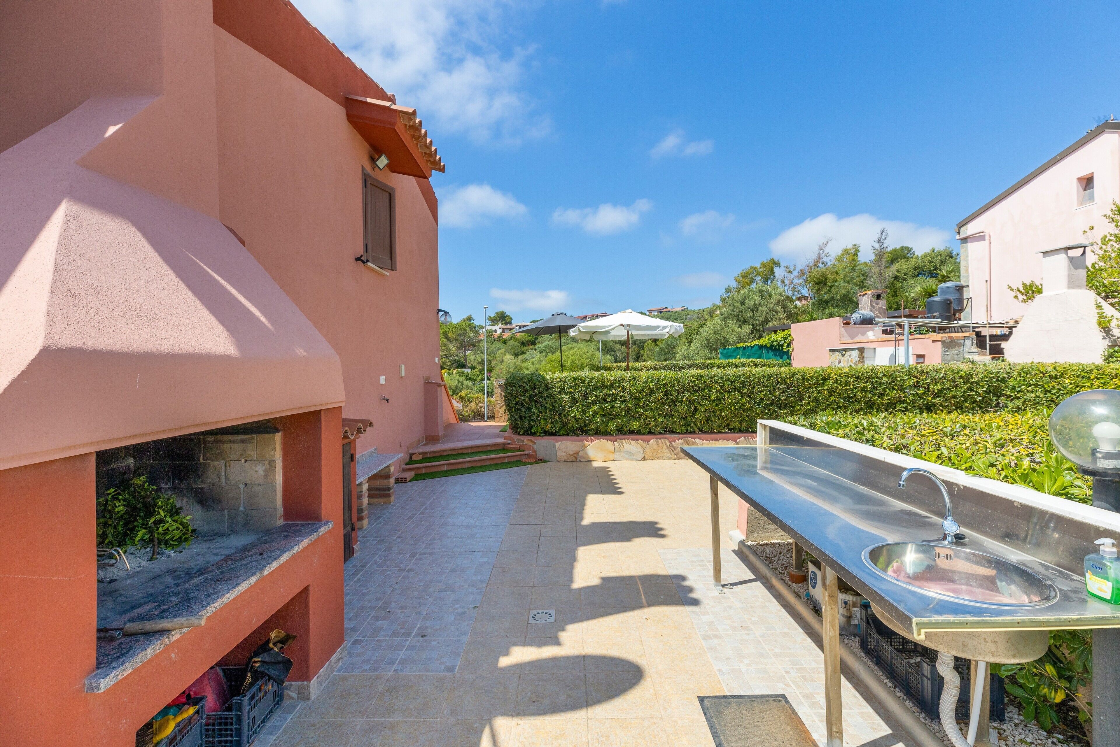 A pink building with a patio area, outdoor sink, and steps leading to a window.