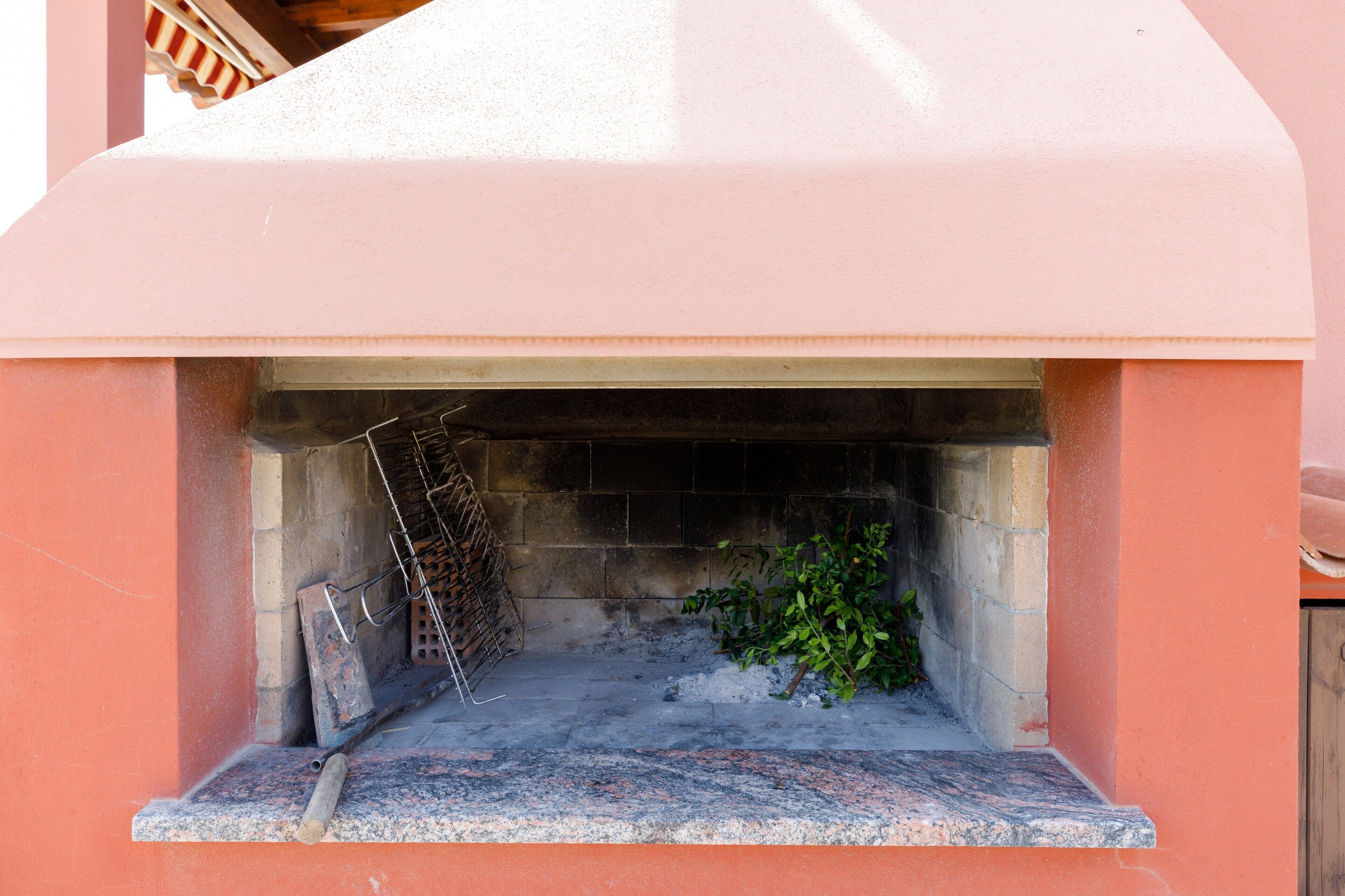 A stone-built outdoor fireplace with a metal grate, surrounded by a red wall.
