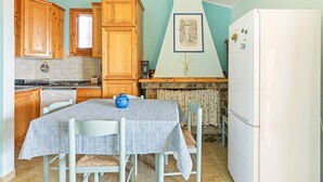 A kitchen with wooden cabinets, a white refrigerator, a dining table with chairs, and a tiled backsplash. - Holiday Home 'Casa Erbì' with Sea View, Private Terrace and Private Garden (Torre dei Corsari Arbus)