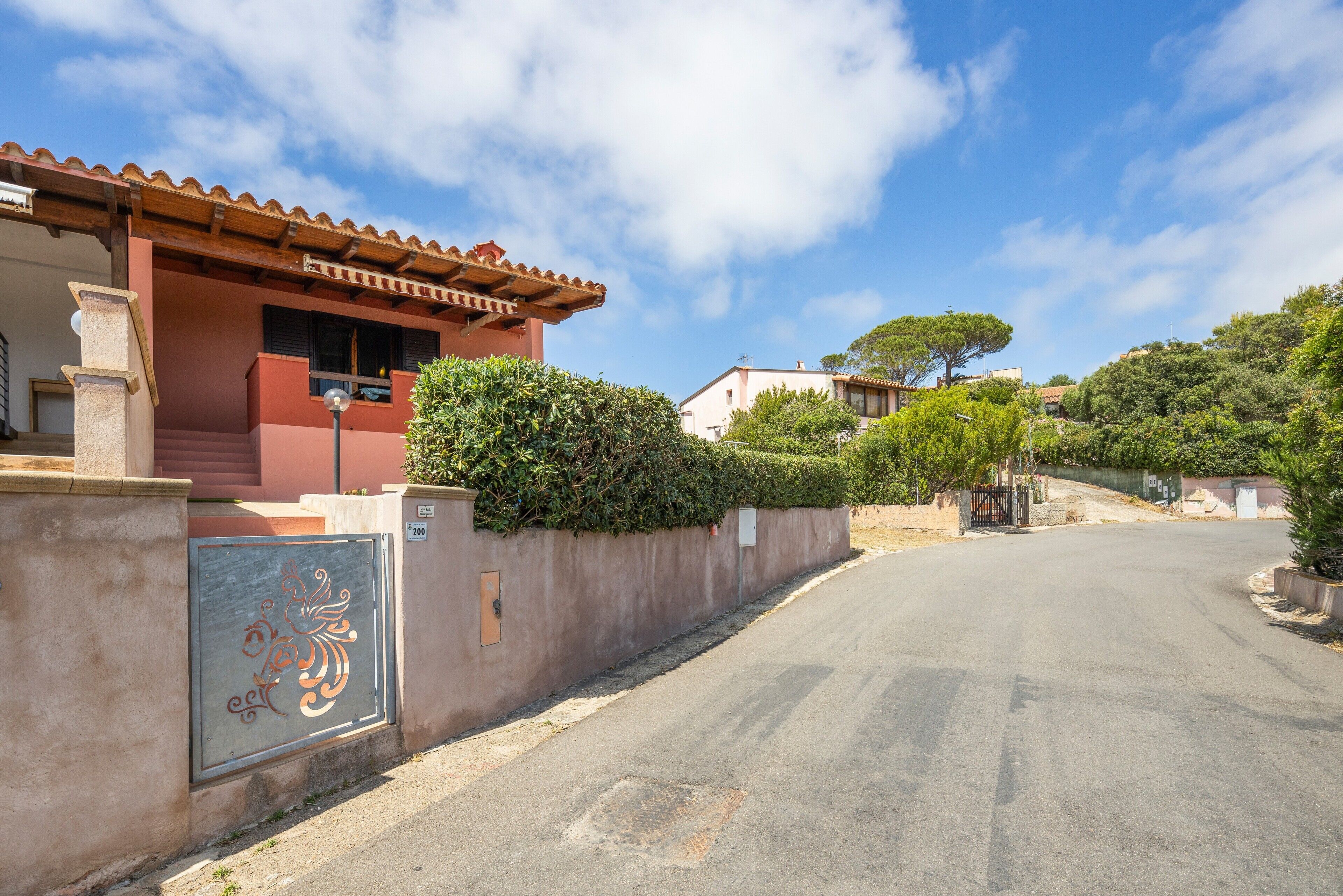 Une rue résidentielle avec une maison rouge, un portail en métal et un ciel dégagé.