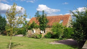A stone building with a sloped roof, surrounded by a grassy yard and trees.