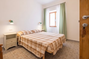 Une chambre à coucher avec un lit, des tables de chevet, une fenêtre avec des rideaux et une porte.