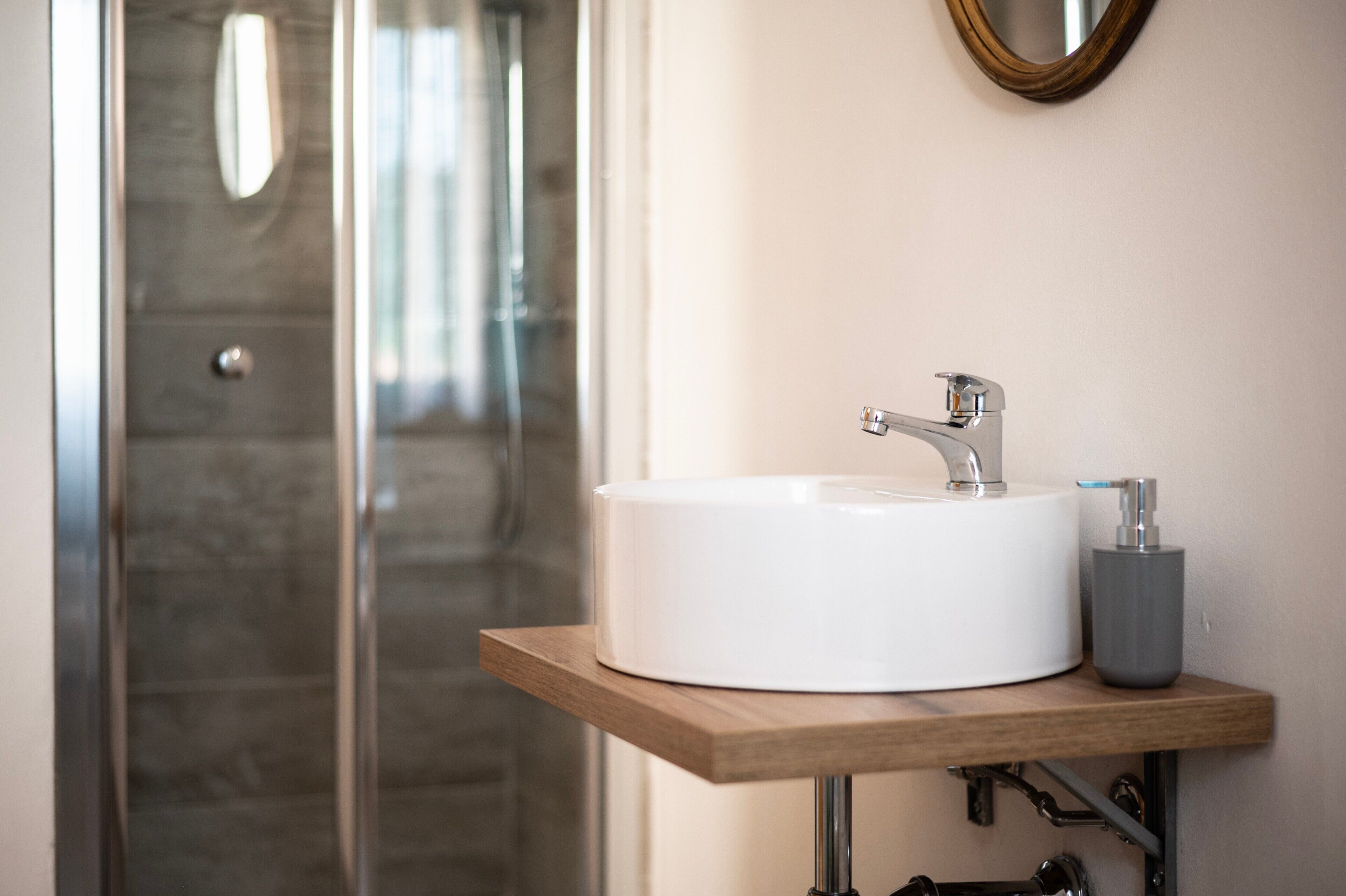 A bathroom with a white sink, a wooden shelf, a mirror, and a shower door.