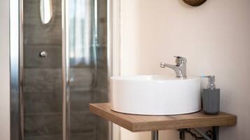 A bathroom with a white sink, a wooden shelf, a mirror, and a shower door.