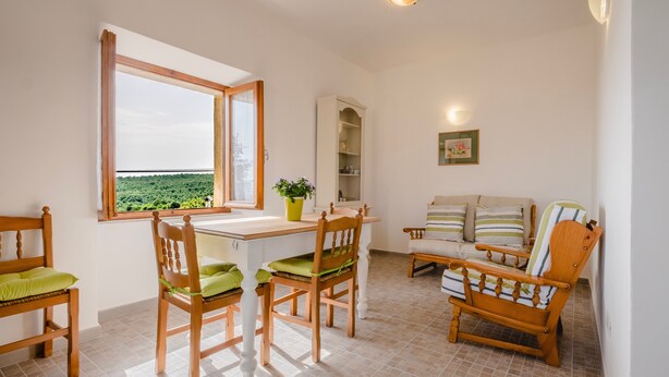 A room with a dining table, chairs, a sofa, a potted plant, and a view of greenery outside. - Apartment "La Sosta del Pellegrino" with Mountain View, Private Garden & Wi-Fi (Sorano)