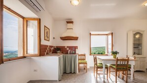A kitchen with a view, a dining area with chairs, and a cabinet. - Apartment "La Sosta del Pellegrino" with Mountain View, Private Garden & Wi-Fi (Sorano)