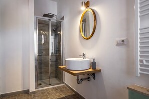Un baño con cabina de ducha de vidrio, un lavamanos blanco y un espejo dorado, además de un perchero.