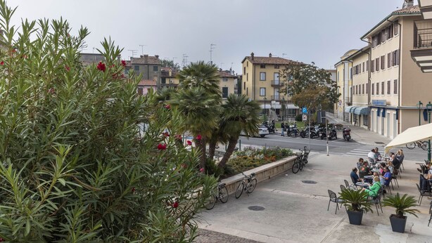 A street view with buildings, outdoor seating, and parked bicycles. - Apartment 'Al Porticciolo' with Sea View, Balcony and Air Conditioning (Grado)