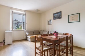 A dining area with a wooden table, chairs, and a window with a view of buildings. - Apartment 'Al Porticciolo' with Sea View, Balcony and Air Conditioning (Grado)