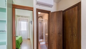 A room with a wooden door, a green bed, a shower area, and a tiled floor. - Apartment 'Al Porticciolo' with Sea View, Balcony and Air Conditioning (Grado)