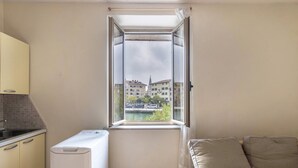 A small room with a window, a washing machine, a bed, and a kitchenette. - Apartment 'Al Porticciolo' with Sea View, Balcony and Air Conditioning (Grado)