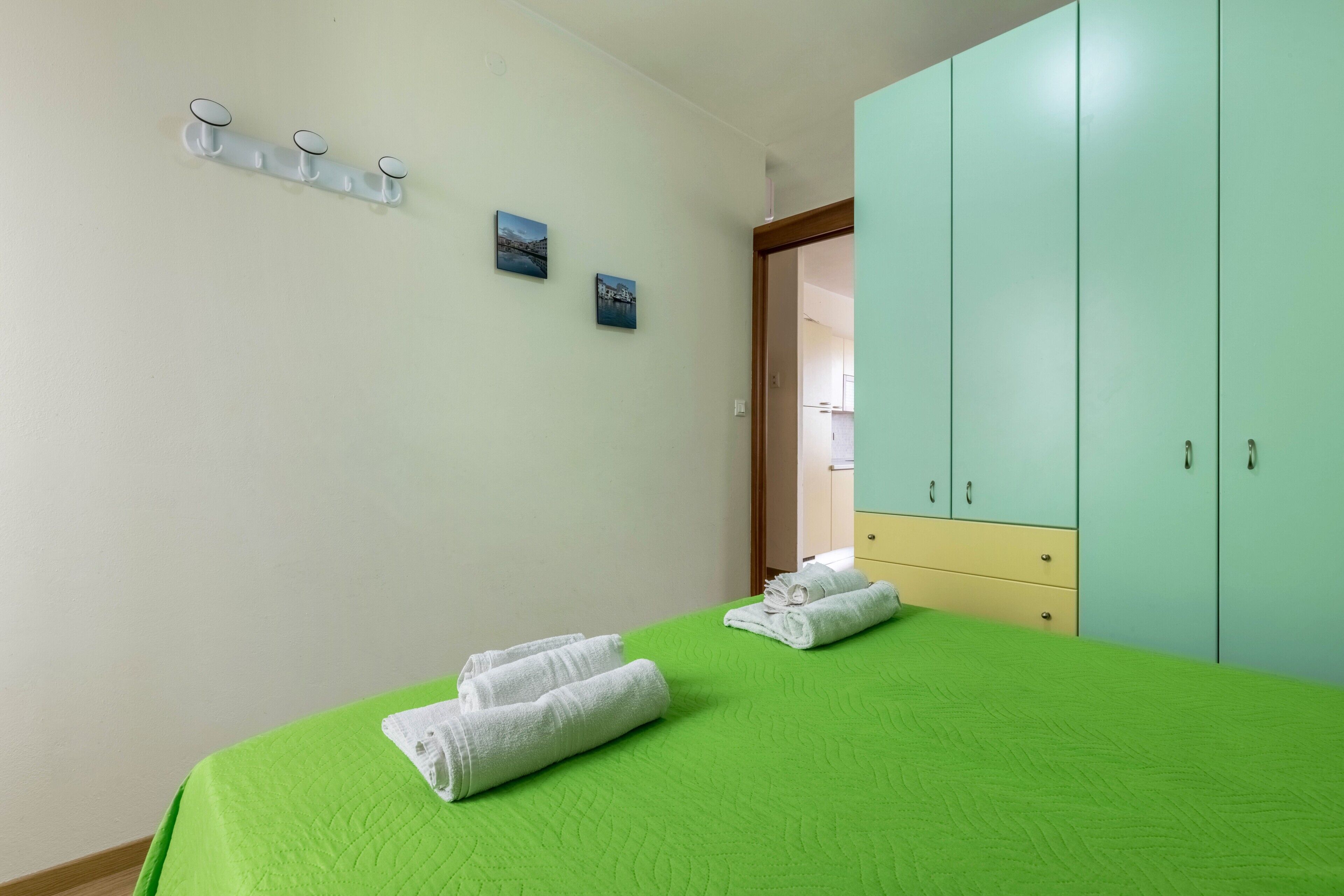 Une chambre avec un lit vert, une armoire et deux crochets fixés au mur.