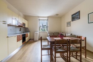A compact kitchen with wooden cabinets, a dining table with chairs, a window with a view, and a small white appliance. - Apartment 'Al Porticciolo' with Sea View, Balcony and Air Conditioning (Grado)