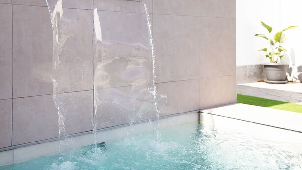 Ein Pool mit klarem Wasser, einem Metallgeländer und einer im Hintergrund stehenden Pflanze in einem Topf.