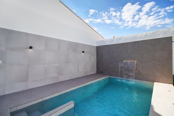 A modern indoor pool with a clear view of the sky, a built-in waterfall feature, and a minimalist design.