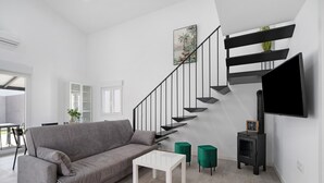 Ein modernes Wohnzimmer mit einem grauen Sofa, einem weißen Couchtisch, grünen Poufs, einem schwarzen Fernseher und einer Treppe mit schwarzen Geländern.