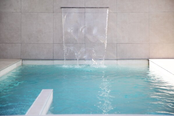 A rectangular pool with clear water, a waterfall feature, and a tiled wall.